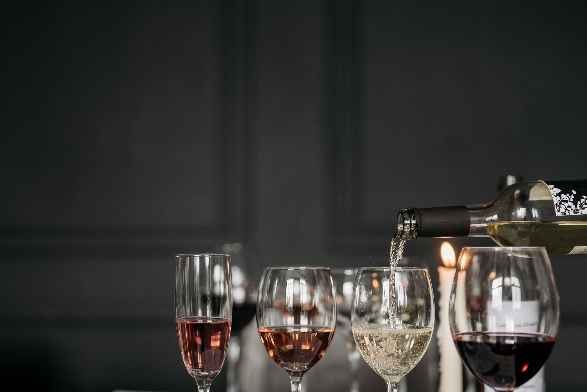 Three wine glasses with red, white, and rosé wine on a dimly lit table setting.